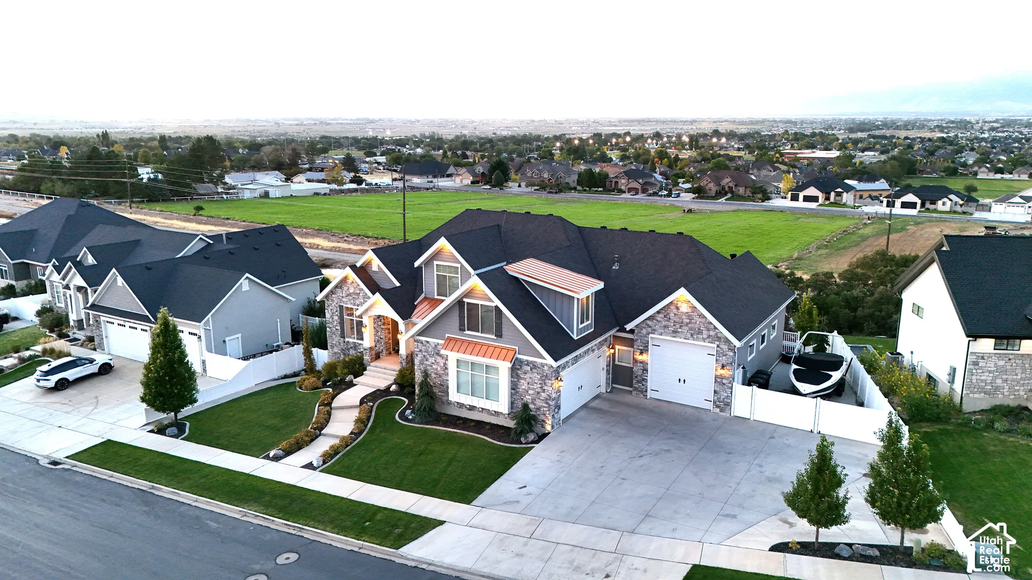 Stone and siding exterior featuring a multi-gabled roof, copper-toned metal roofing accents, a curved concrete walkway, and an attached three-car garage