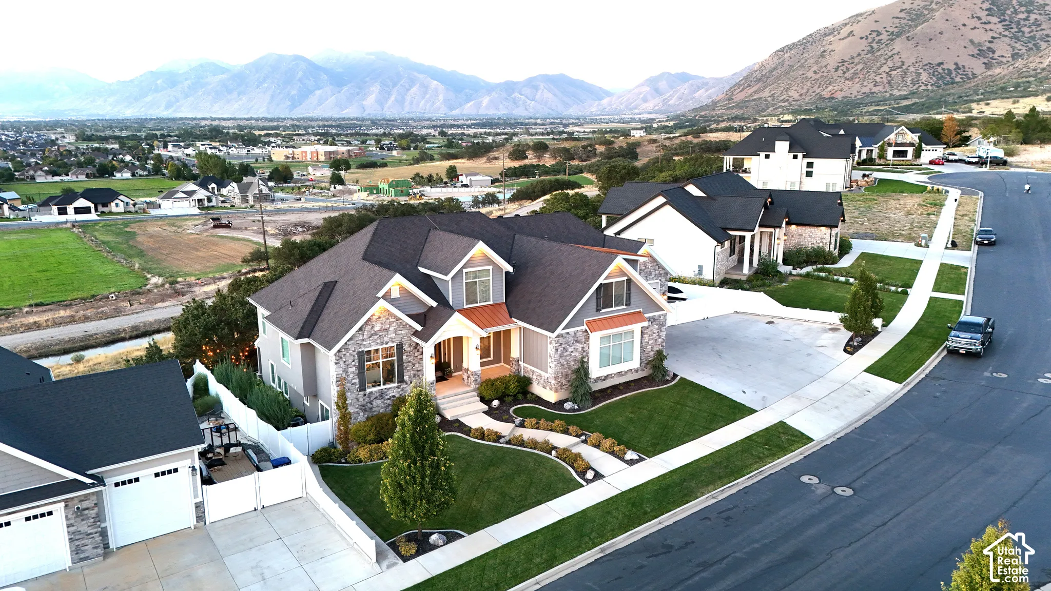 Multi-level residence featuring a stone and siding exterior, asphalt shingle roof, concrete driveway, manicured landscaping, and mountain backdrop