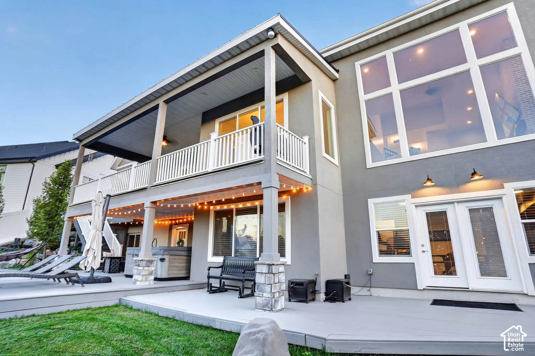Two-story exterior featuring multi-level decking, an upper-level covered balcony with white railings, expansive windows, and stone-accented support pillars