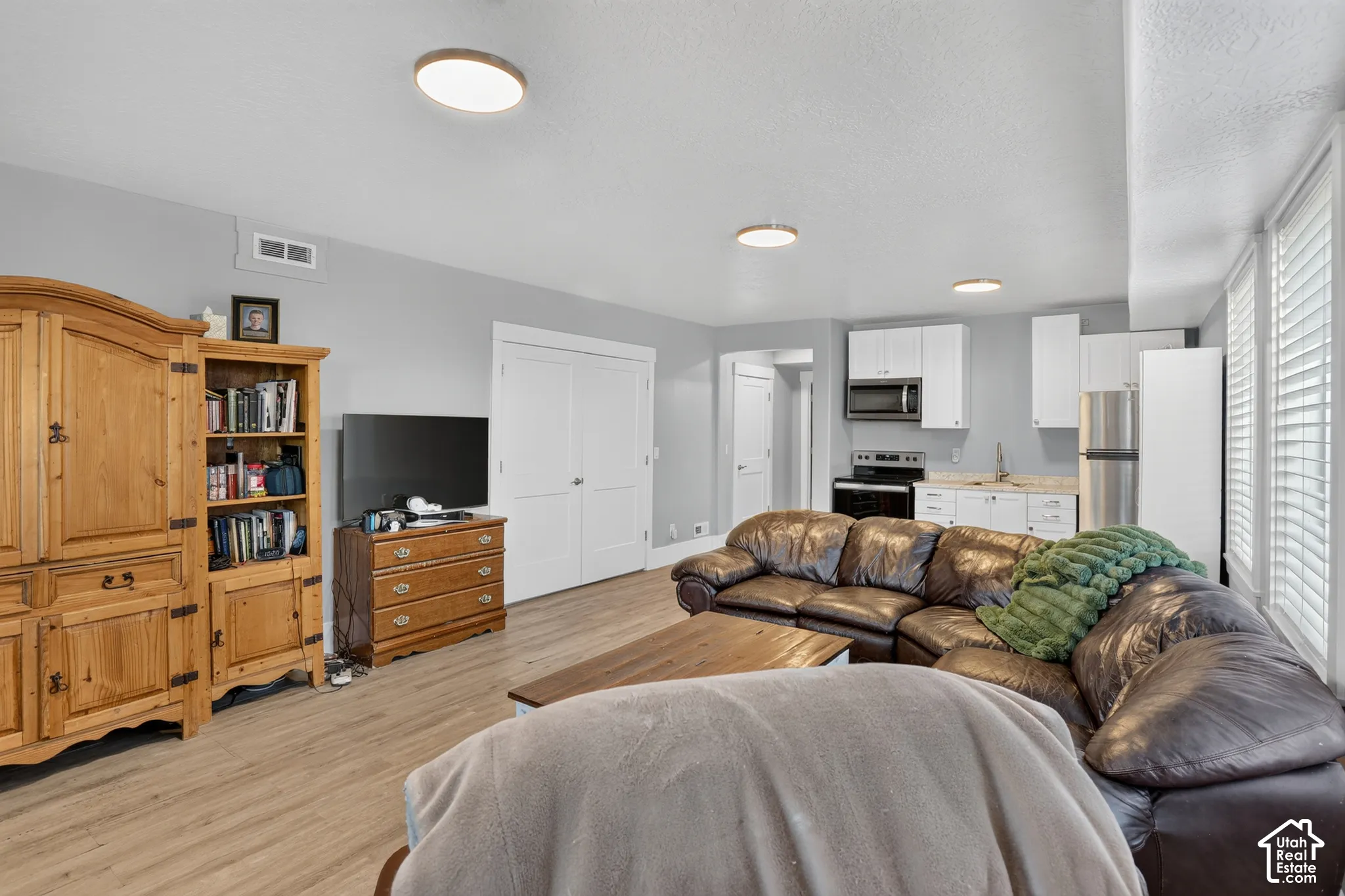 Wood-finish flooring, white cabinetry with stone-surface countertops, stainless steel kitchen appliances, and flush-mount ceiling lighting
