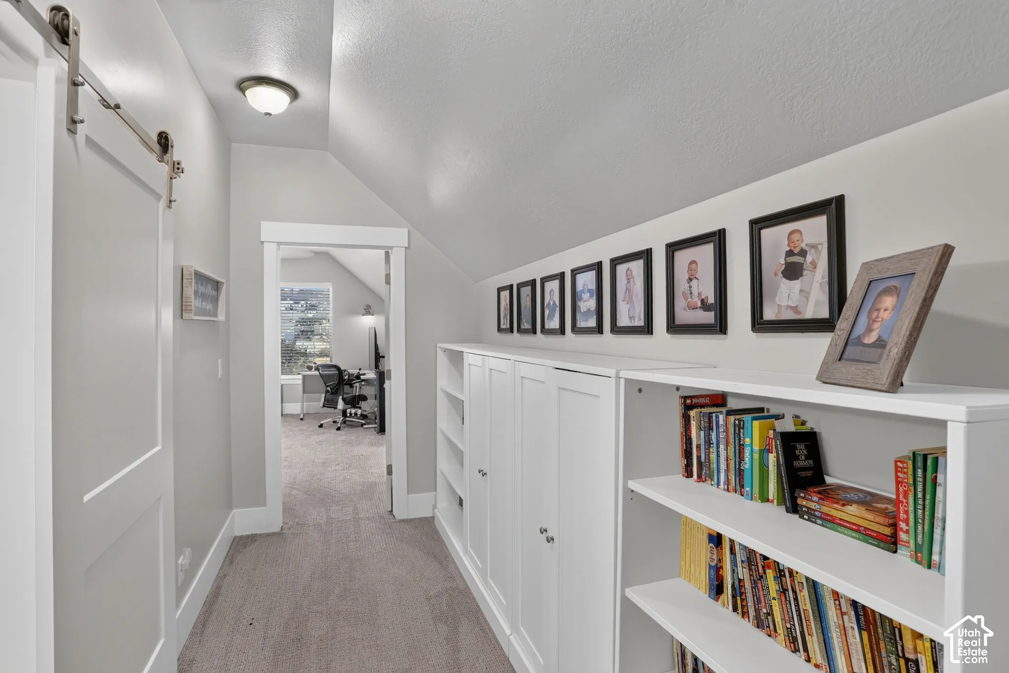 Custom white built-in cabinetry featuring open shelving and enclosed storage, sliding barn-style door, and sloped ceiling architecture