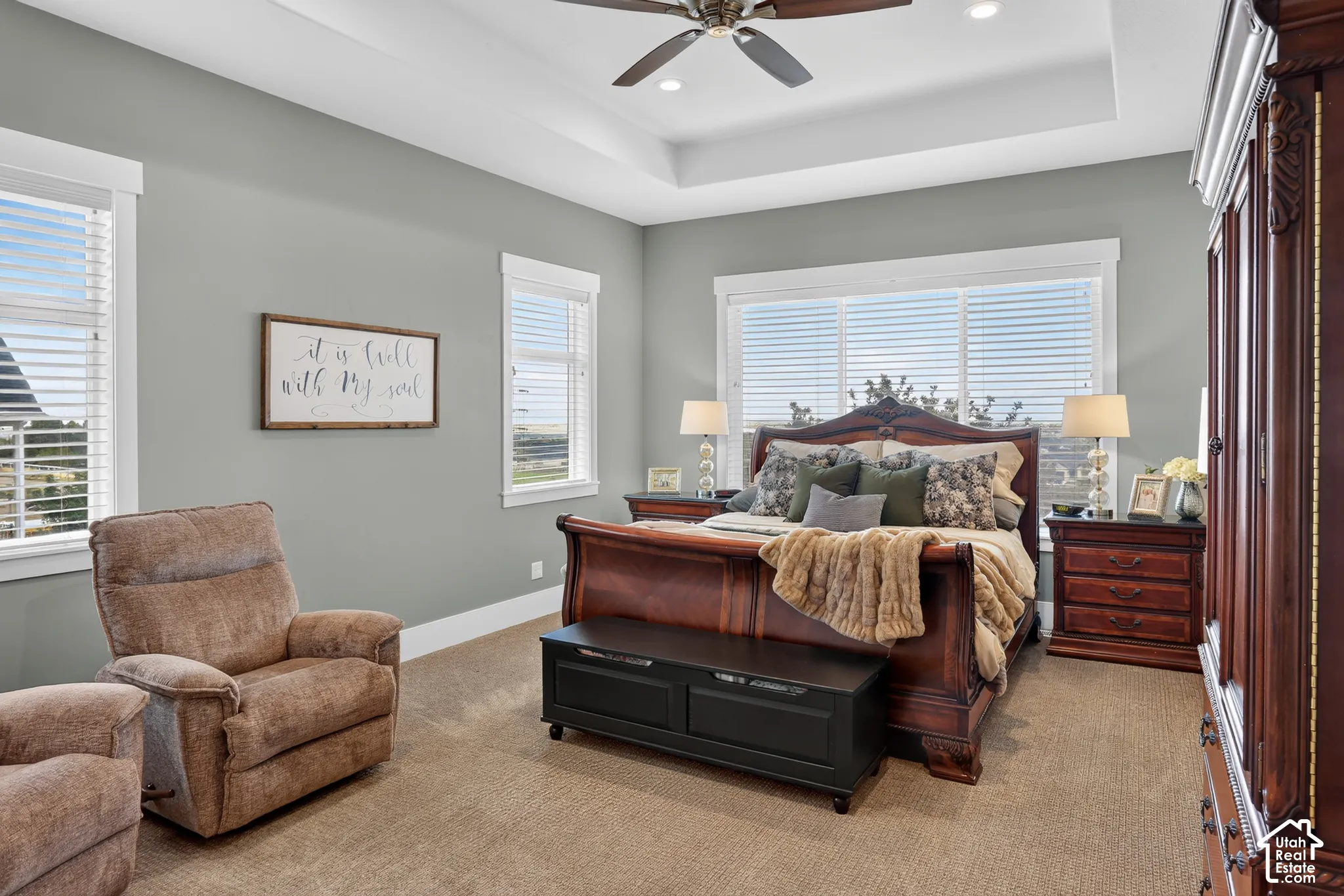 Tray ceiling with recessed lighting, ceiling fan, multiple windows with neutral blinds, and wall-to-wall carpeting