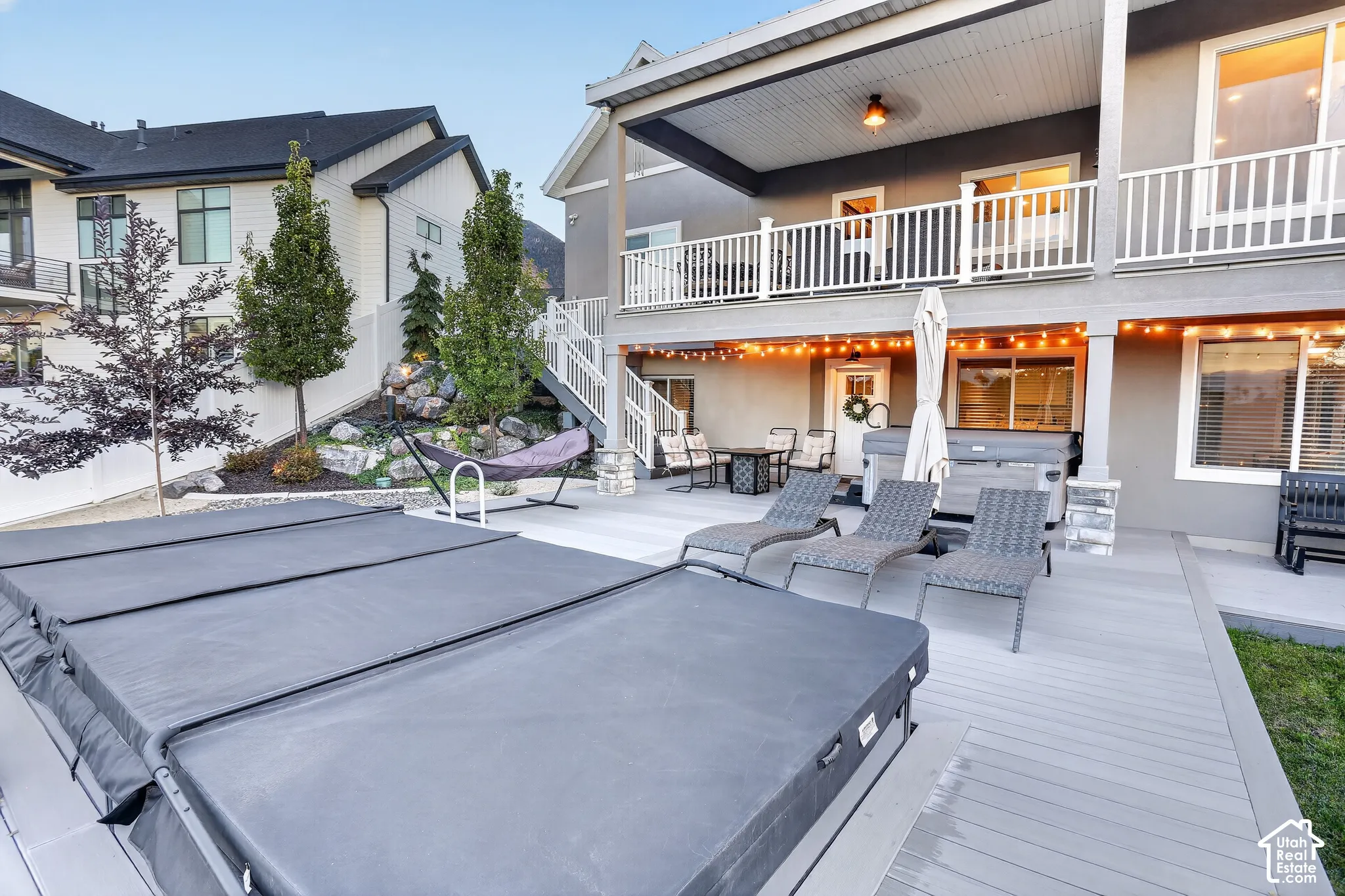 Rear exterior featuring a multi-level deck, covered patio space, built-in hot tub, and stone-accented landscaping with mature trees