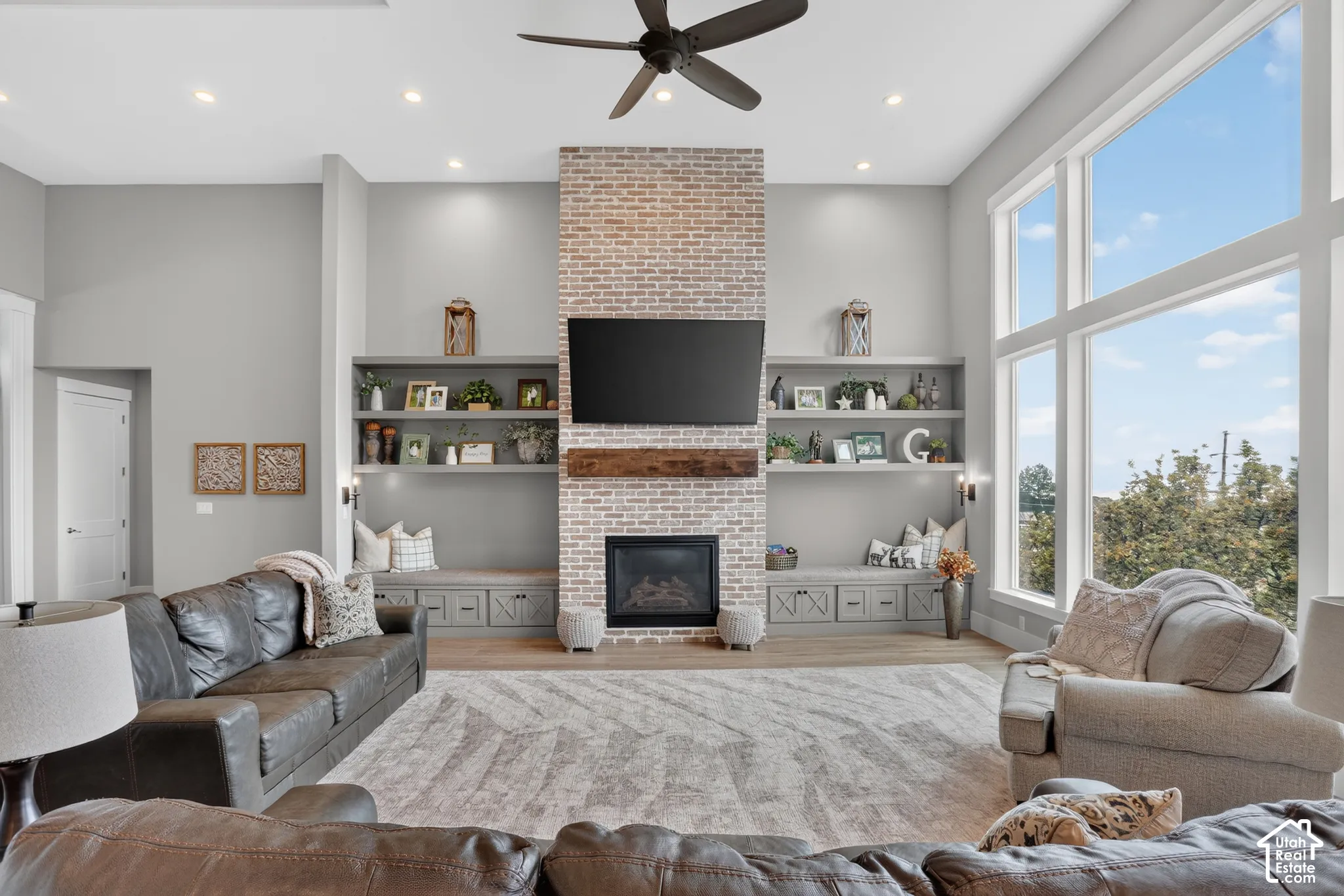 High-ceiling interior featuring a floor-to-ceiling brick fireplace, natural wood mantel, custom built-in cabinetry with bench seating, and expansive multi-panel windows