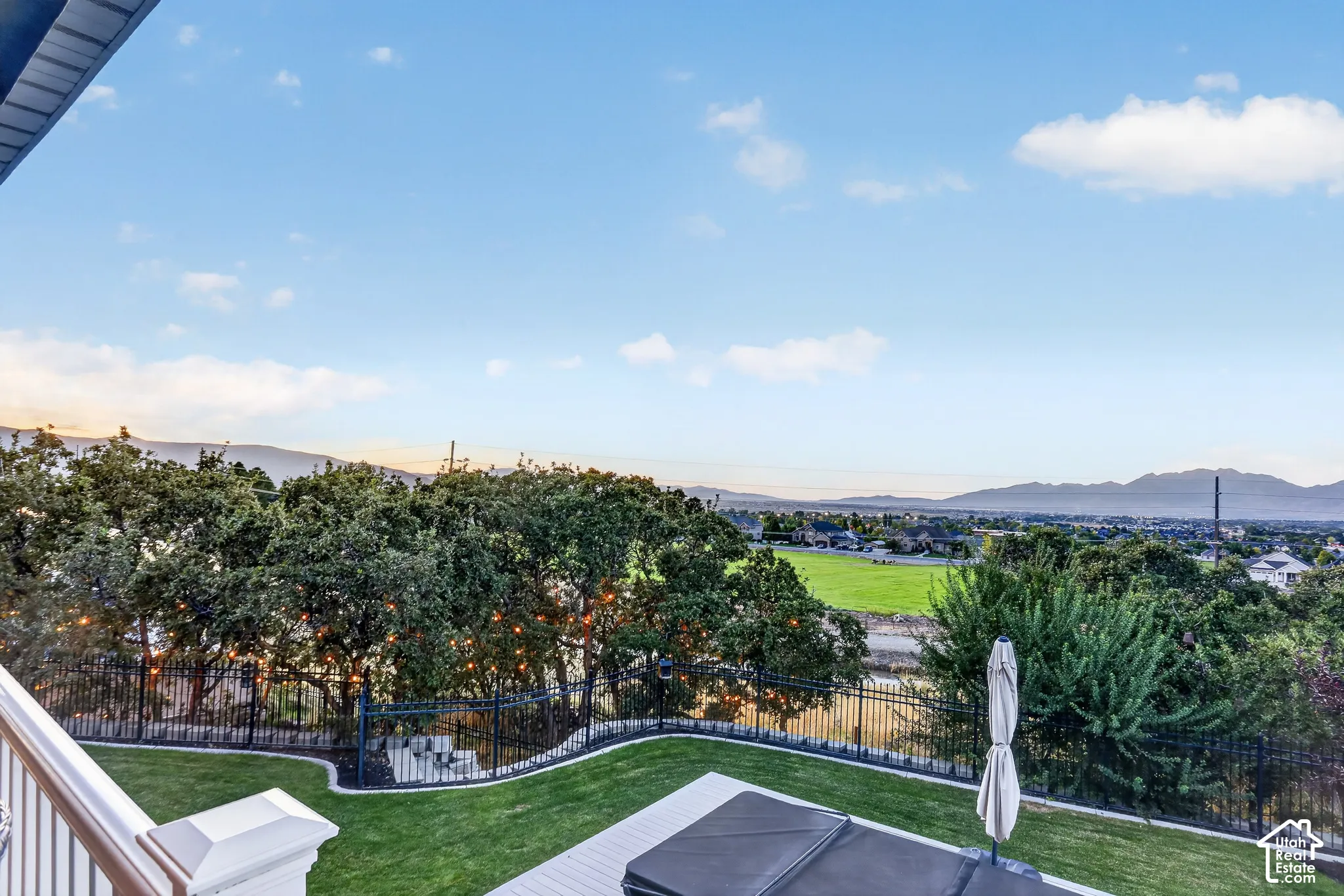 Elevated deck featuring a white railing and perimeter metal fencing overlooking a manicured lawn and distant mountain landscape