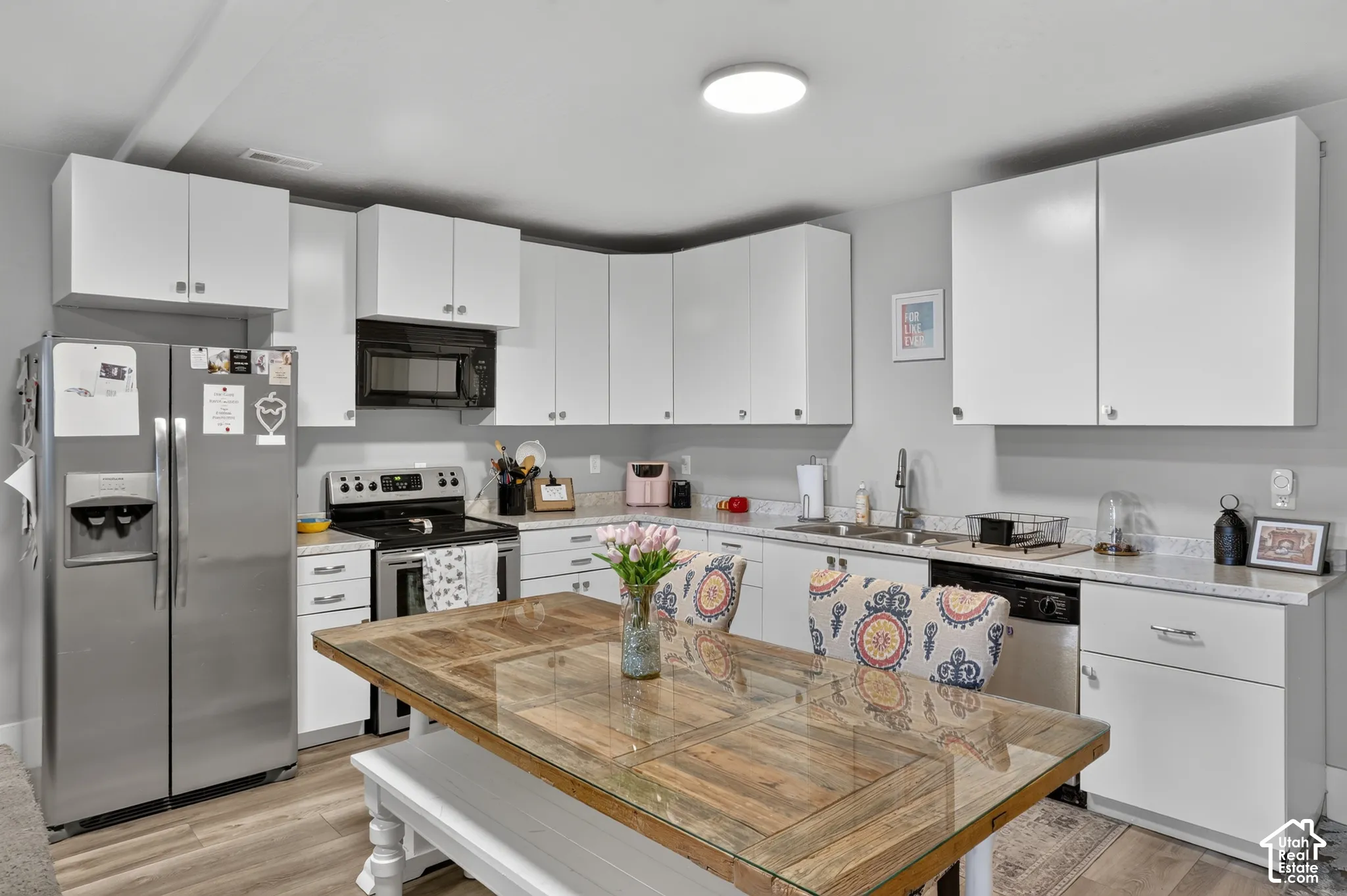 Kitchen featuring white flat-panel cabinetry, light-toned stone-finish countertops, wood-finish flooring, and stainless steel appliances