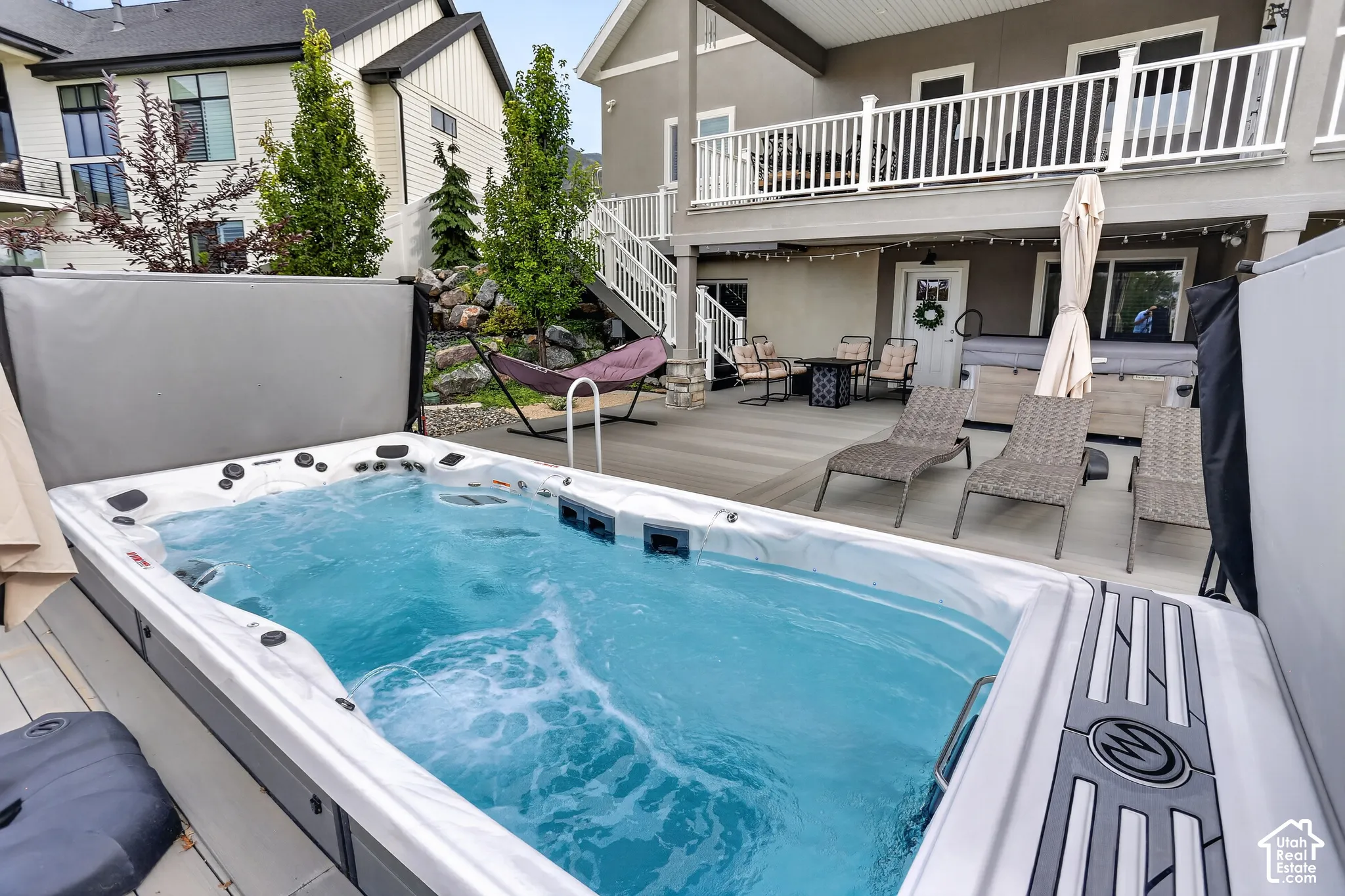 Backyard featuring a swim spa, composite decking, upper-level balcony with white railings, and tiered landscaping