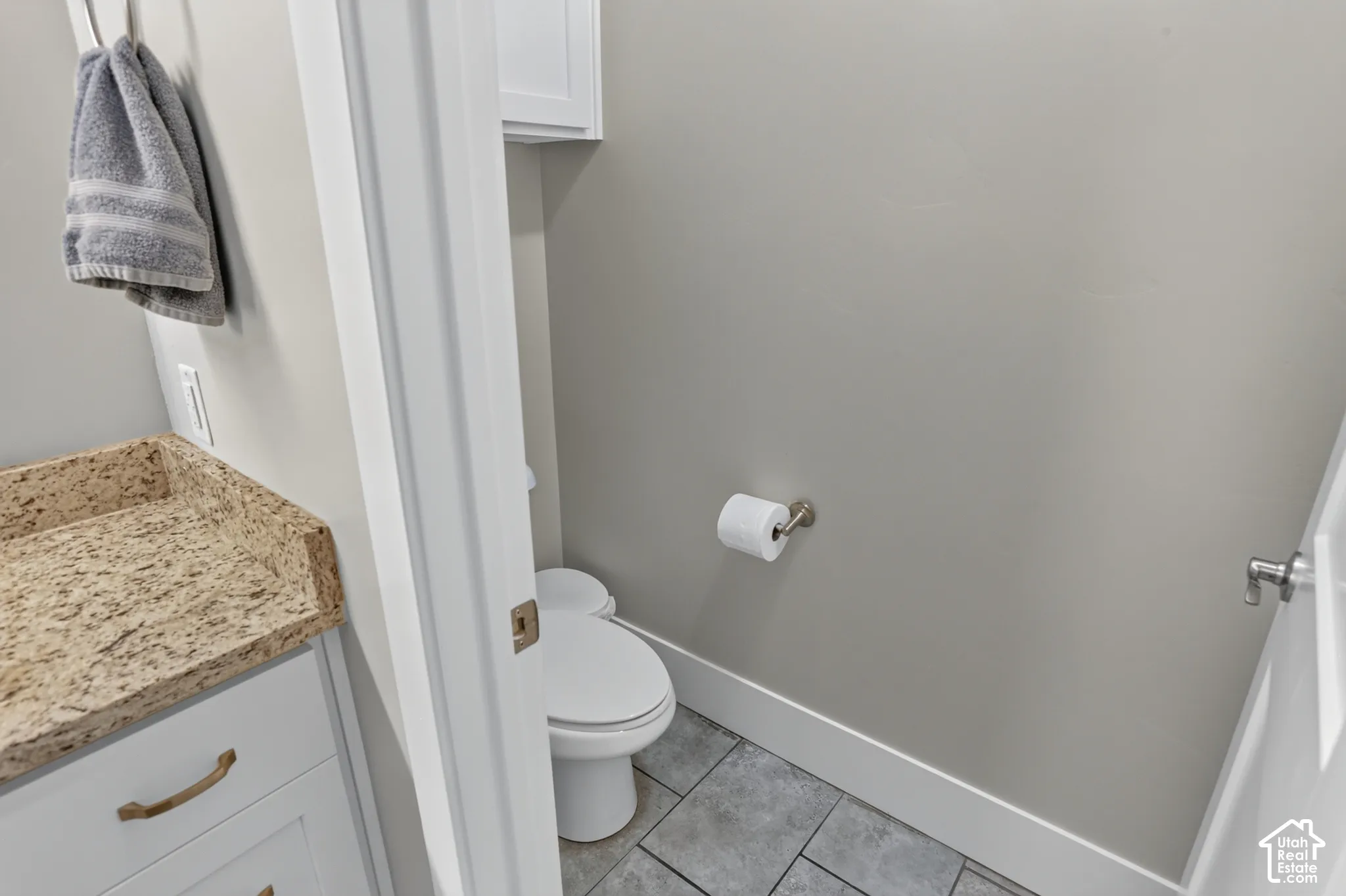 Vanity with stone countertop, white shaker-style cabinetry, matte hardware, tile flooring, and wall-mounted toilet