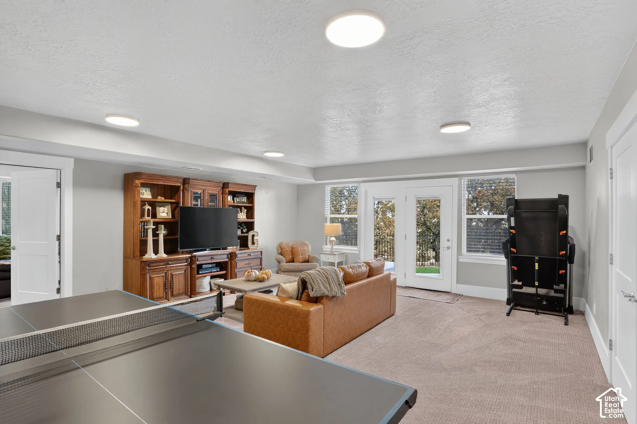 Multi-purpose room featuring neutral carpeting, built-in wooden cabinetry, recessed ceiling lighting, and glass-paneled double doors providing exterior access