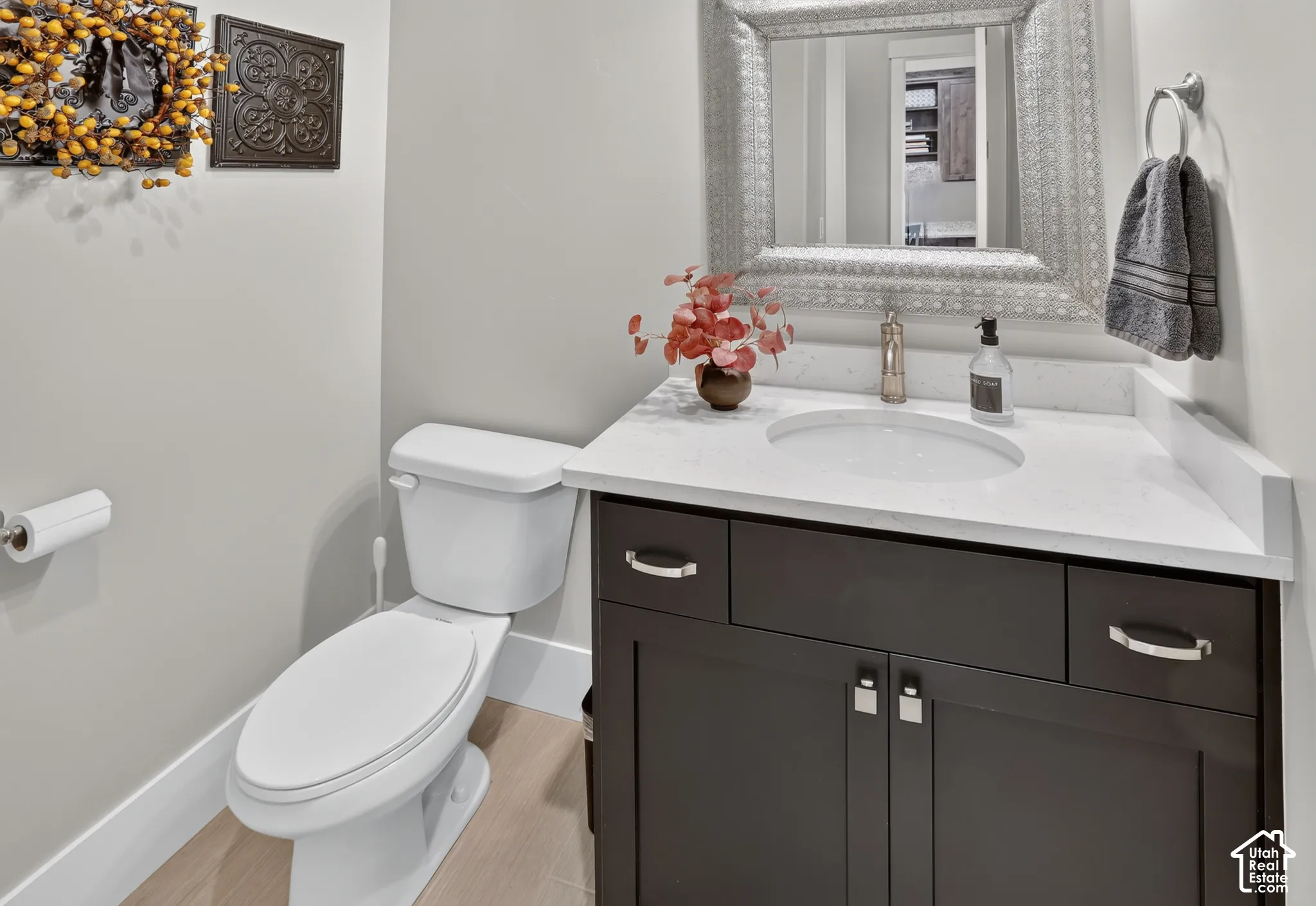 Vanity featuring dark cabinetry, a light-toned stone-composite countertop, an integrated oval basin, metallic hardware, and wood-finish flooring