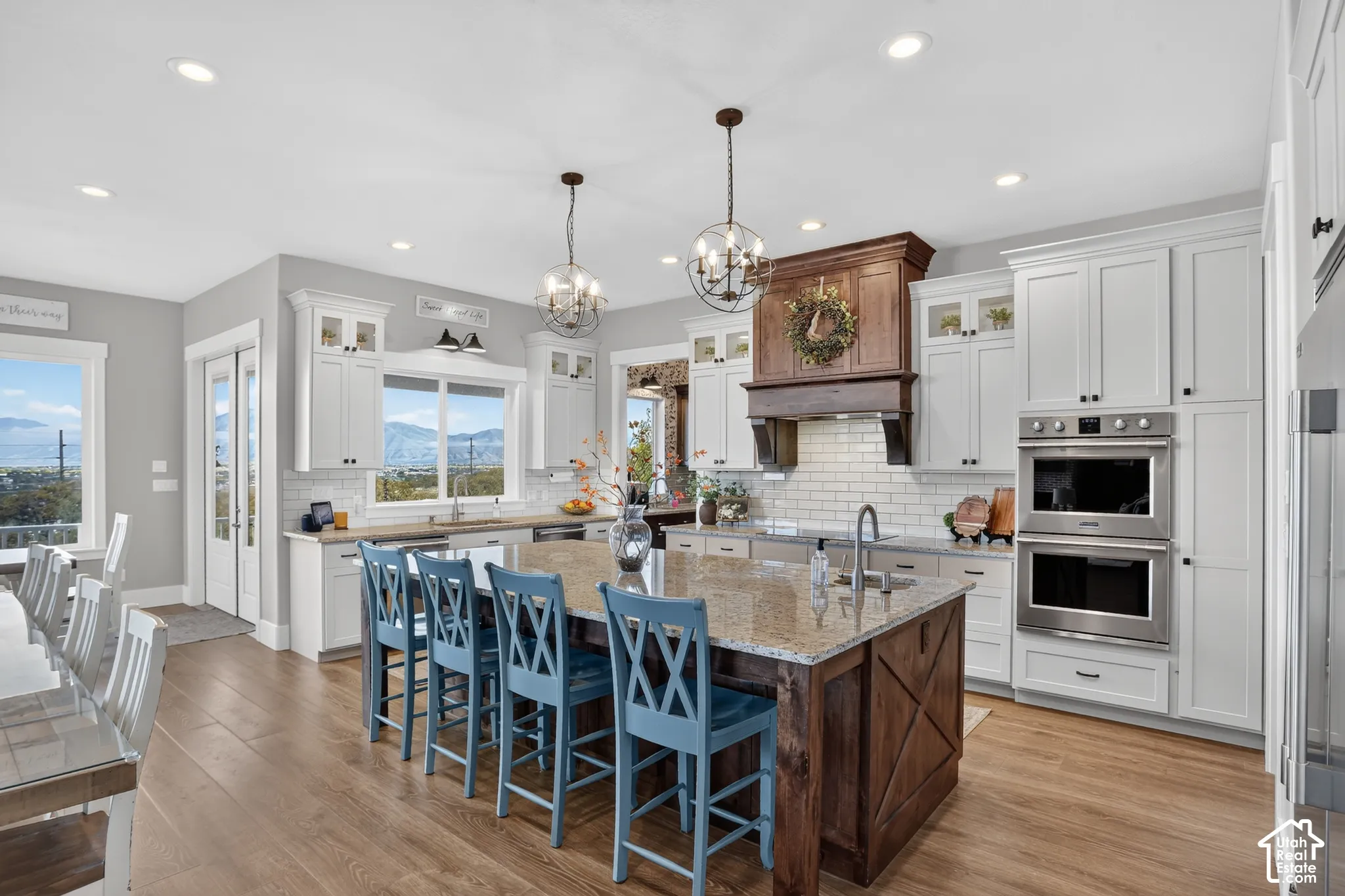 Kitchen featuring white shaker-style cabinetry, central island with a wood-finish base, stone countertop, stainless steel double wall oven, and pendant lighting