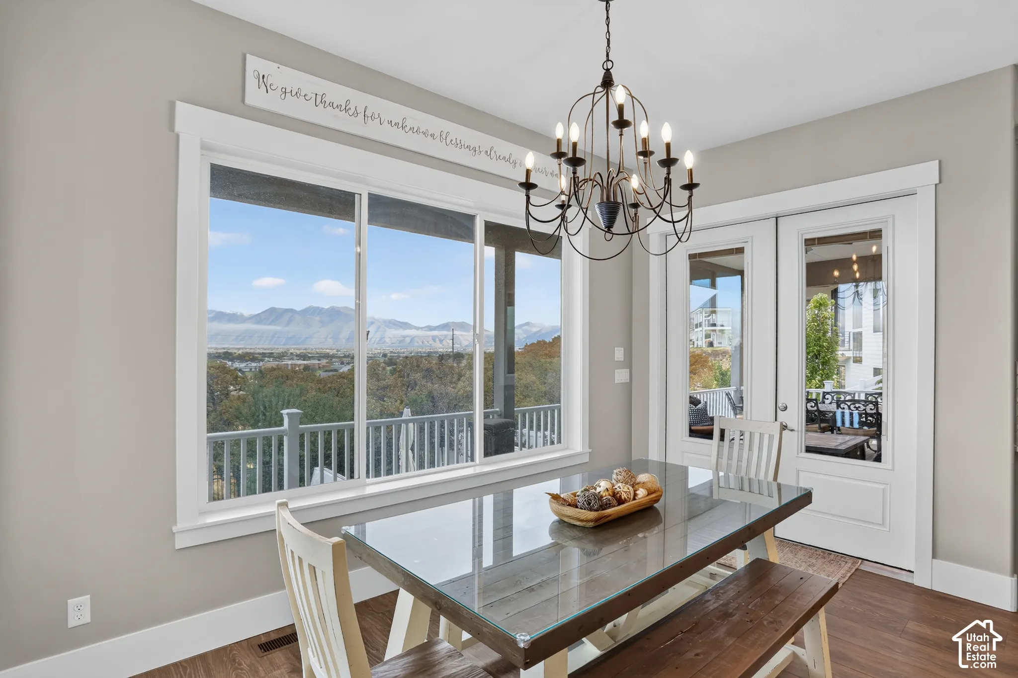 Dining area featuring wood-finish flooring, a decorative iron chandelier, a large picture window, and a glass-paneled exterior door showcasing mountain scenery