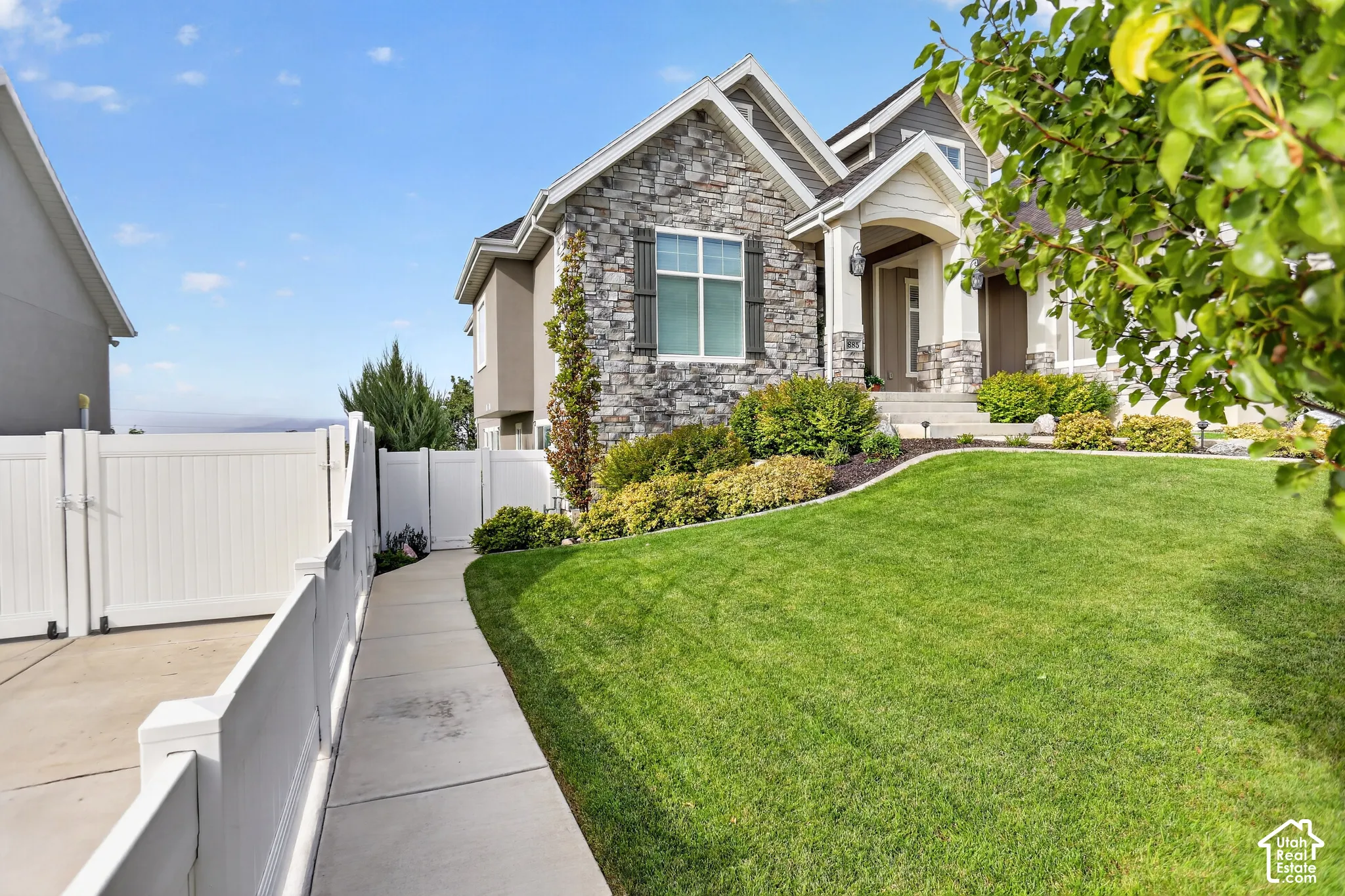 Exterior facade featuring stone veneer masonry, dual-gabled rooflines, decorative shutters, a covered entryway, and a vinyl privacy fence