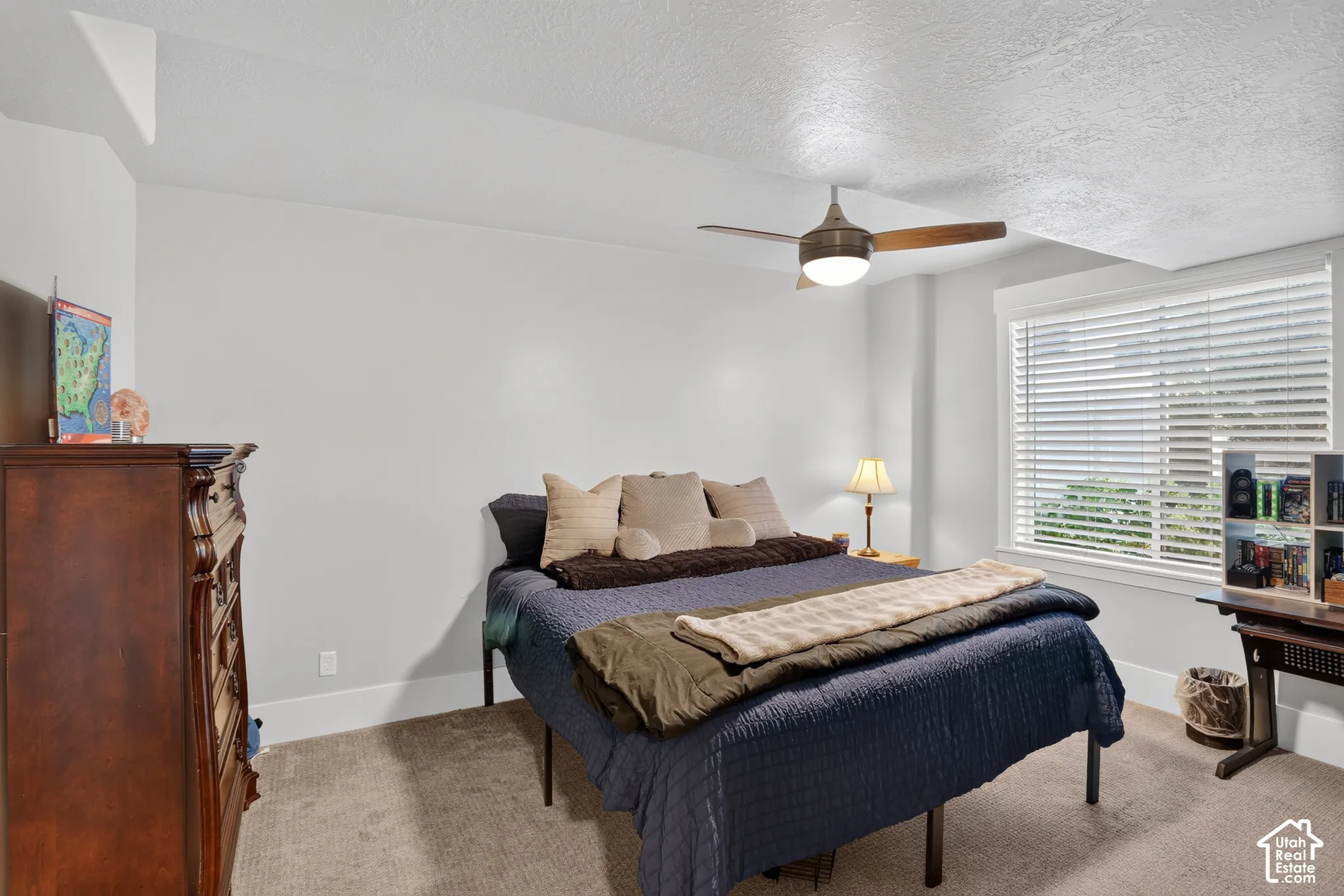 Neutral interior space featuring wall-to-wall carpeting, a multi-blade ceiling fan with integrated lighting, and a large window equipped with horizontal slat blinds