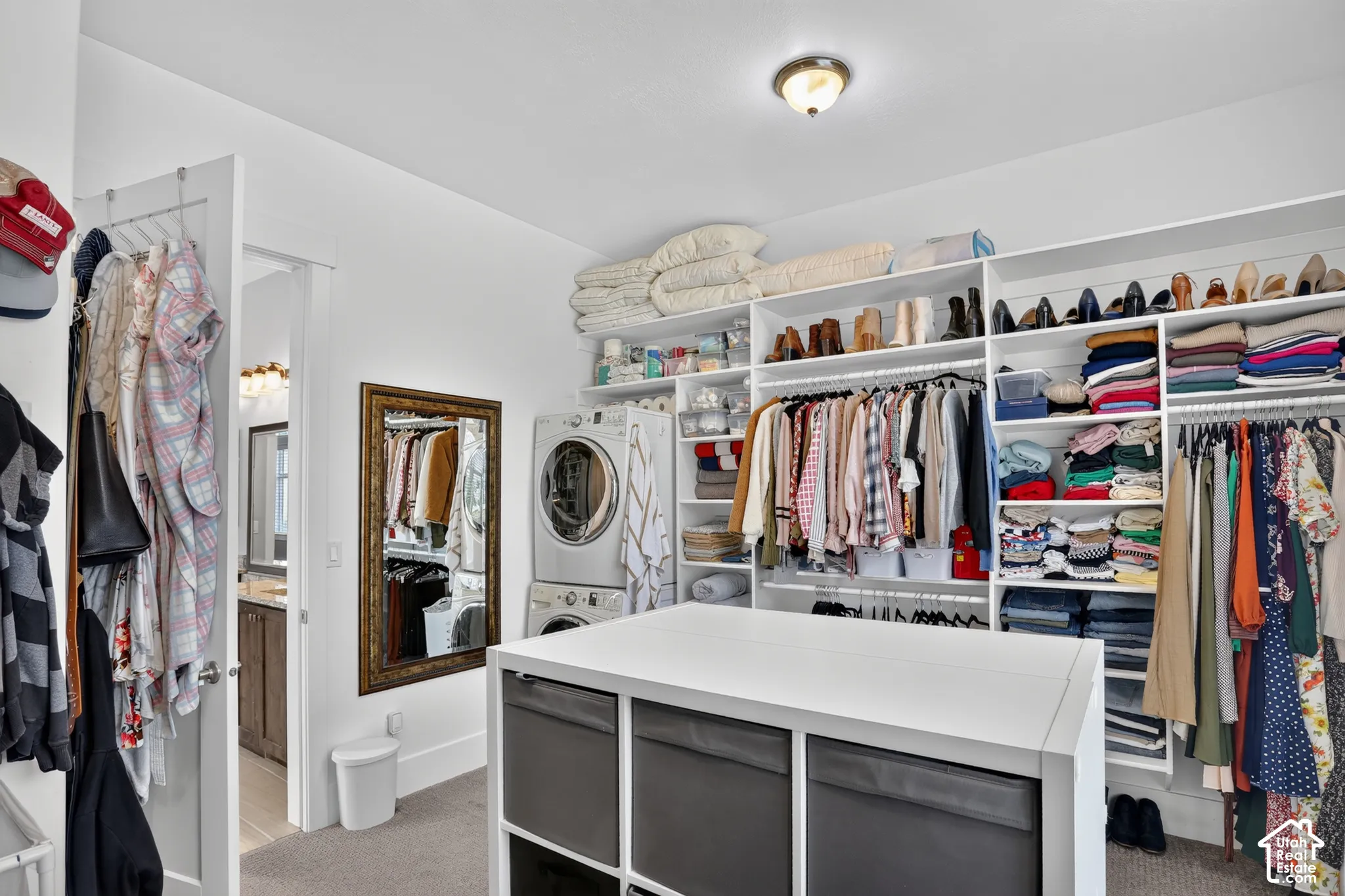 Walk-in closet featuring extensive built-in white shelving, integrated laundry station with stacked washer and dryer, and a central built-in storage island