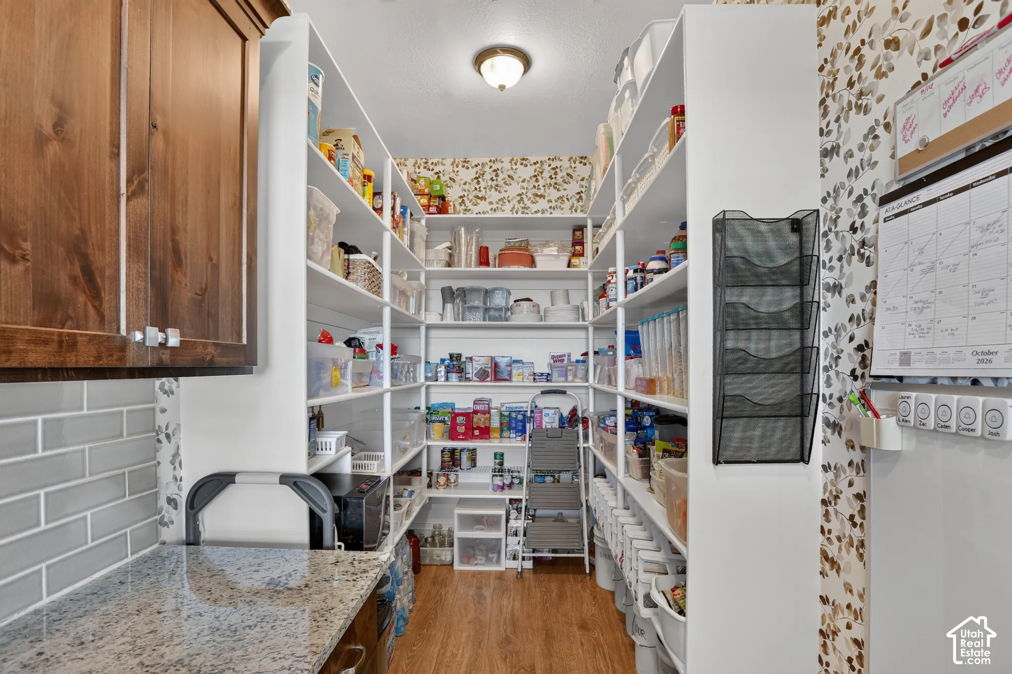 Pantry featuring custom white built-in shelving, wood-finish flooring, stone-surfaced countertop, and subway tile backsplash
