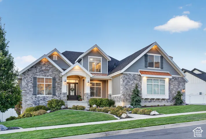 Multi-gabled exterior featuring stone veneer siding, horizontal lap accents, copper-toned metal roofing details, and a covered entry with a glass-paneled front door