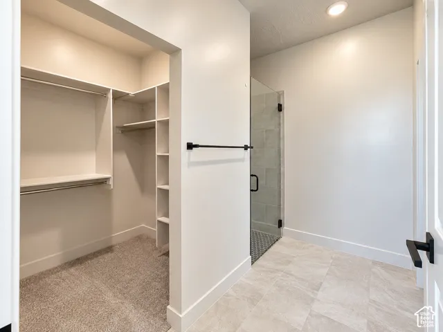 Walk-in closet featuring built-in shelving and hanging rods, tiled floor shower enclosure with a glass door, matte black hardware, and neutral-tone tile flooring