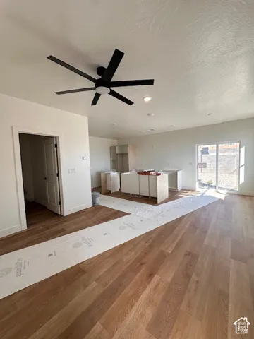 Open-concept interior featuring wood-finish flooring, a matte black multi-blade ceiling fan, recessed lighting, white cabinetry, and sliding glass doors