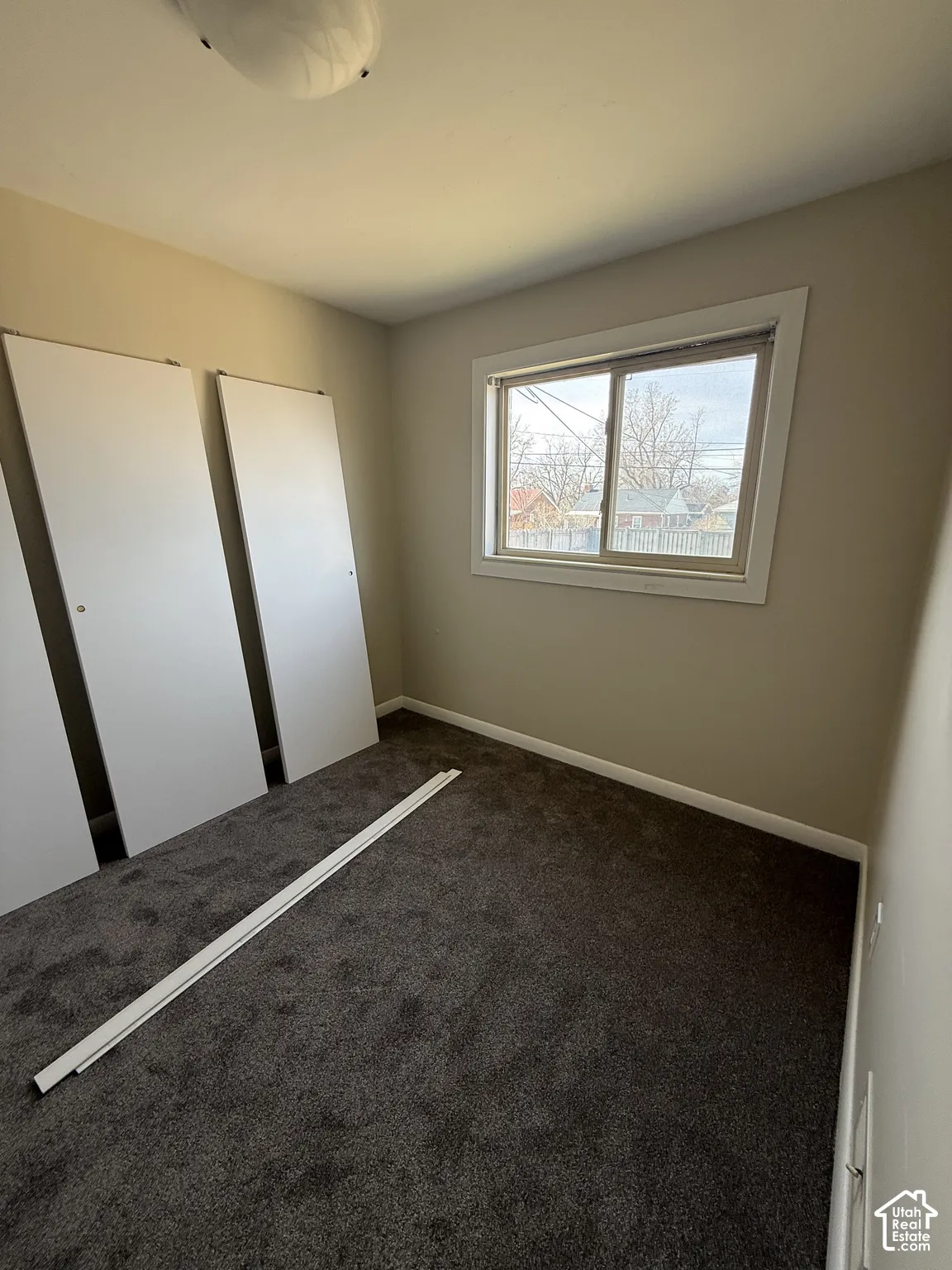 Room featuring neutral-toned walls, dark-toned carpeting, a sliding window, and two built-in closet doors