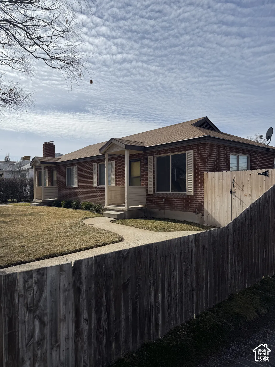 Brick exterior featuring dual covered entries, an exposed masonry chimney, and a fenced side perimeter