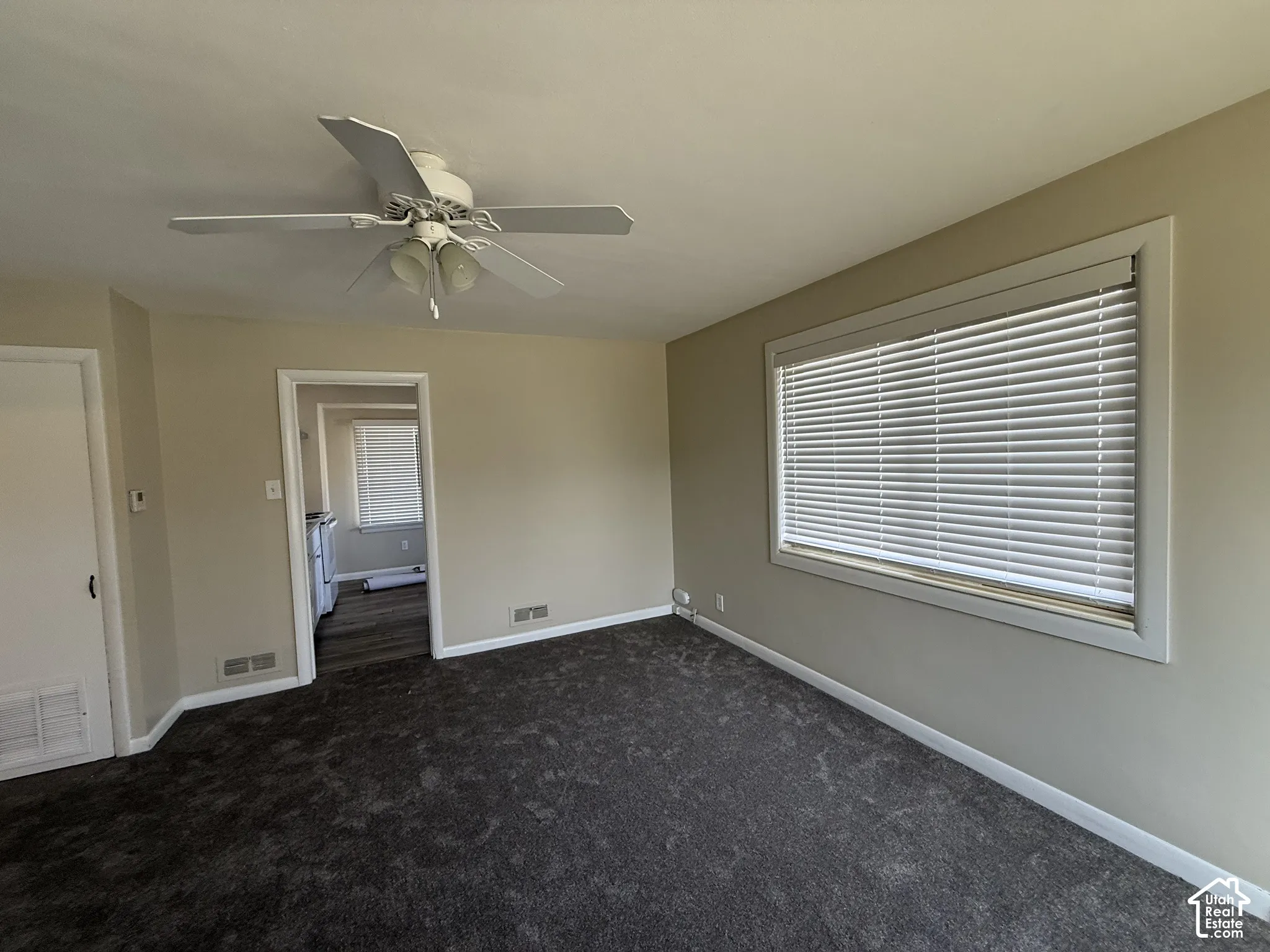 Neutral-toned interior featuring wall-to-wall carpeting, a multi-blade ceiling fan with integrated lighting, and a large horizontal window equipped with horizontal blinds