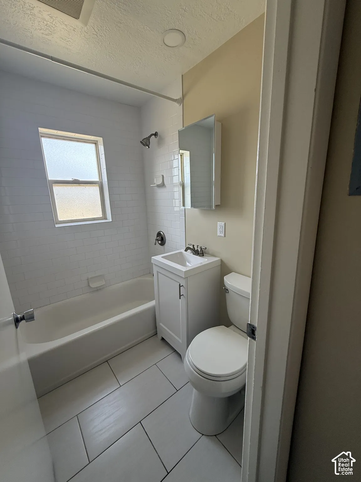 Bathroom featuring a white subway tile shower surround, porcelain floor tile, single-basin vanity cabinet, and wall-mounted medicine cabinet