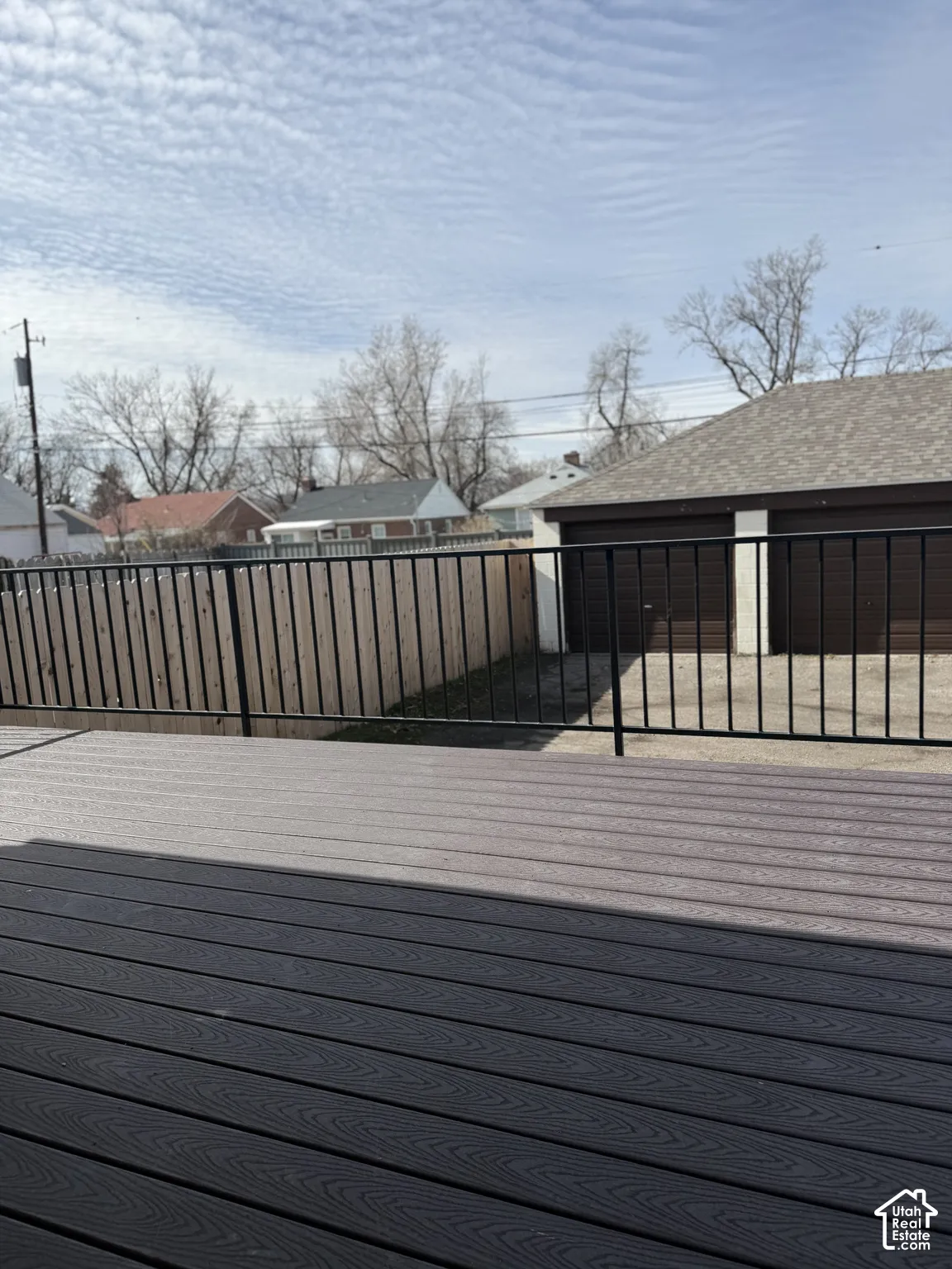 Composite deck featuring a black metal railing, wood-tone privacy fencing, and a detached two-car garage