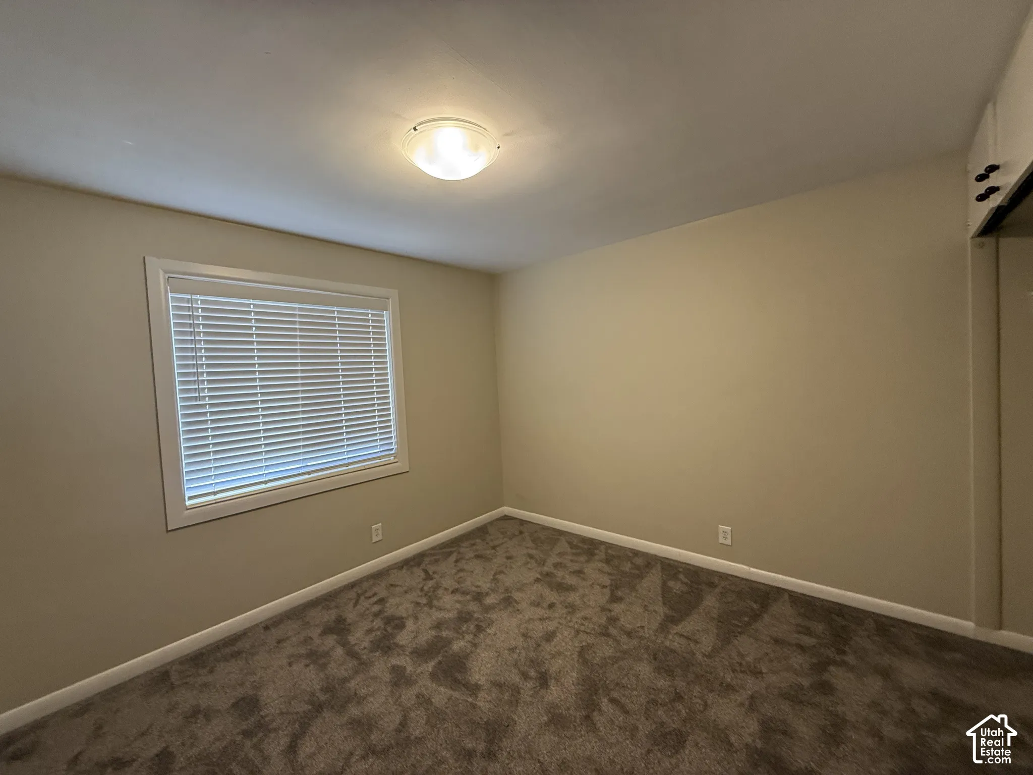 Neutral-toned interior room featuring wall-to-wall carpeting, a large window with fitted blinds, and a built-in closet with sliding doors