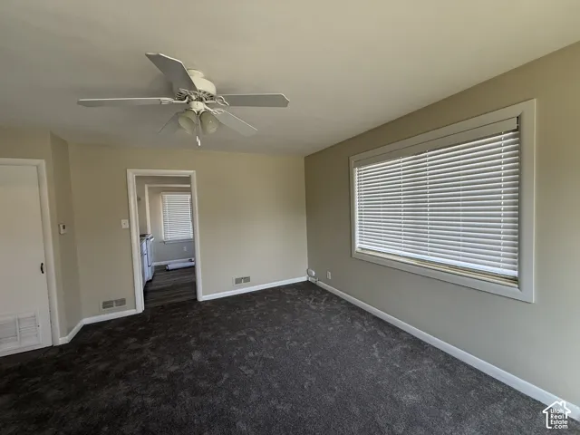 Neutral-toned interior featuring wall-to-wall carpeting, a multi-blade ceiling fan with integrated lighting, and a large horizontal window equipped with horizontal blinds
