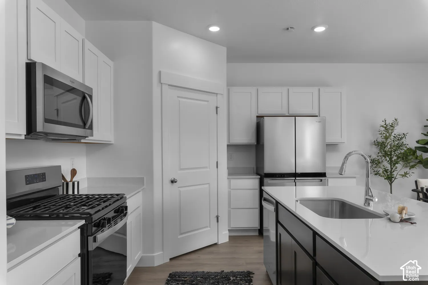 Kitchen featuring white shaker-style cabinetry, a contrasting dark-finish kitchen island, solid-surface countertops, stainless steel appliances, and wood-finish flooring