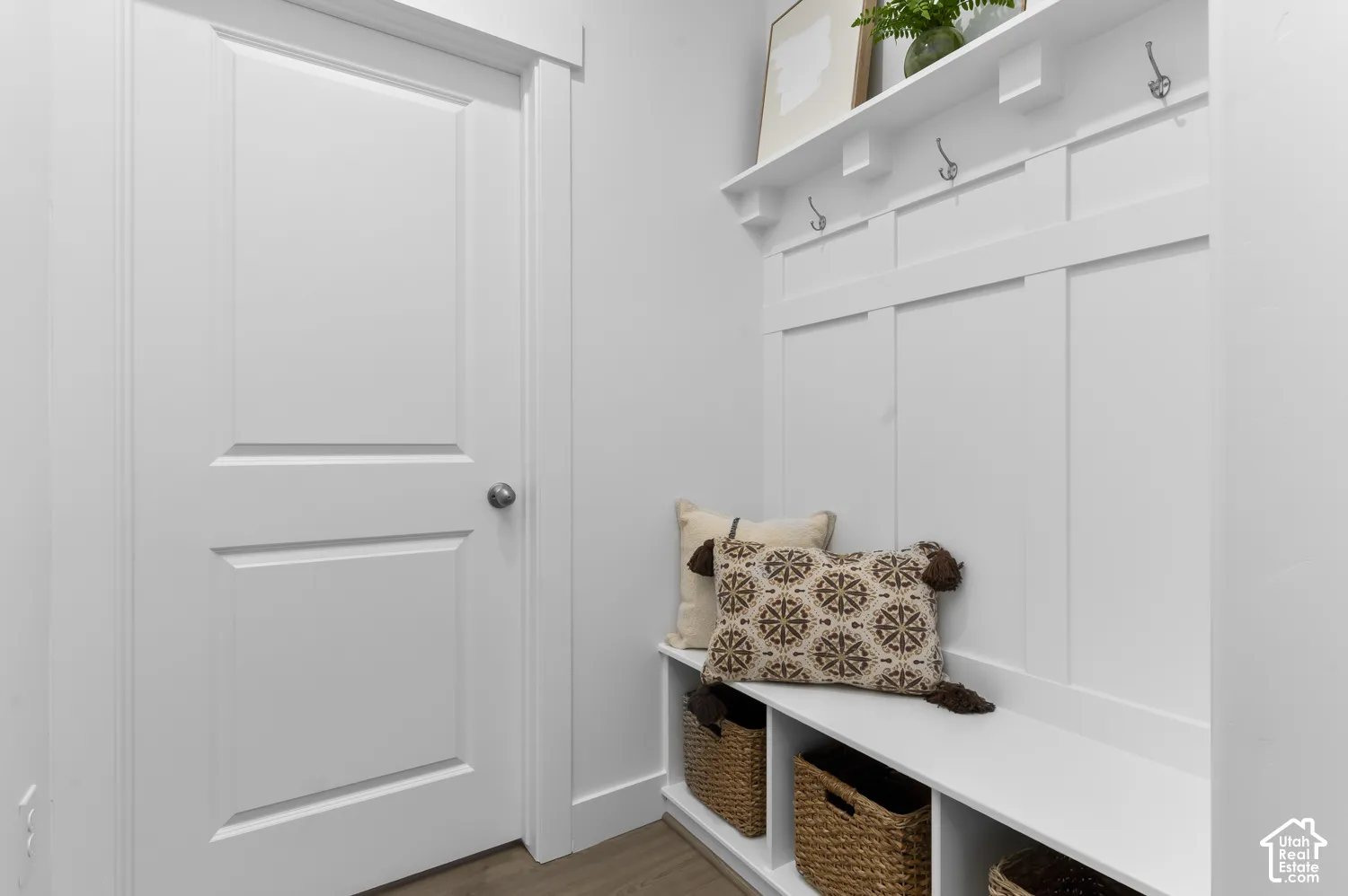 Built-in mudroom bench with integrated storage cubbies, white board-and-batten wall paneling, fixed upper shelf, and brushed metal wall hooks