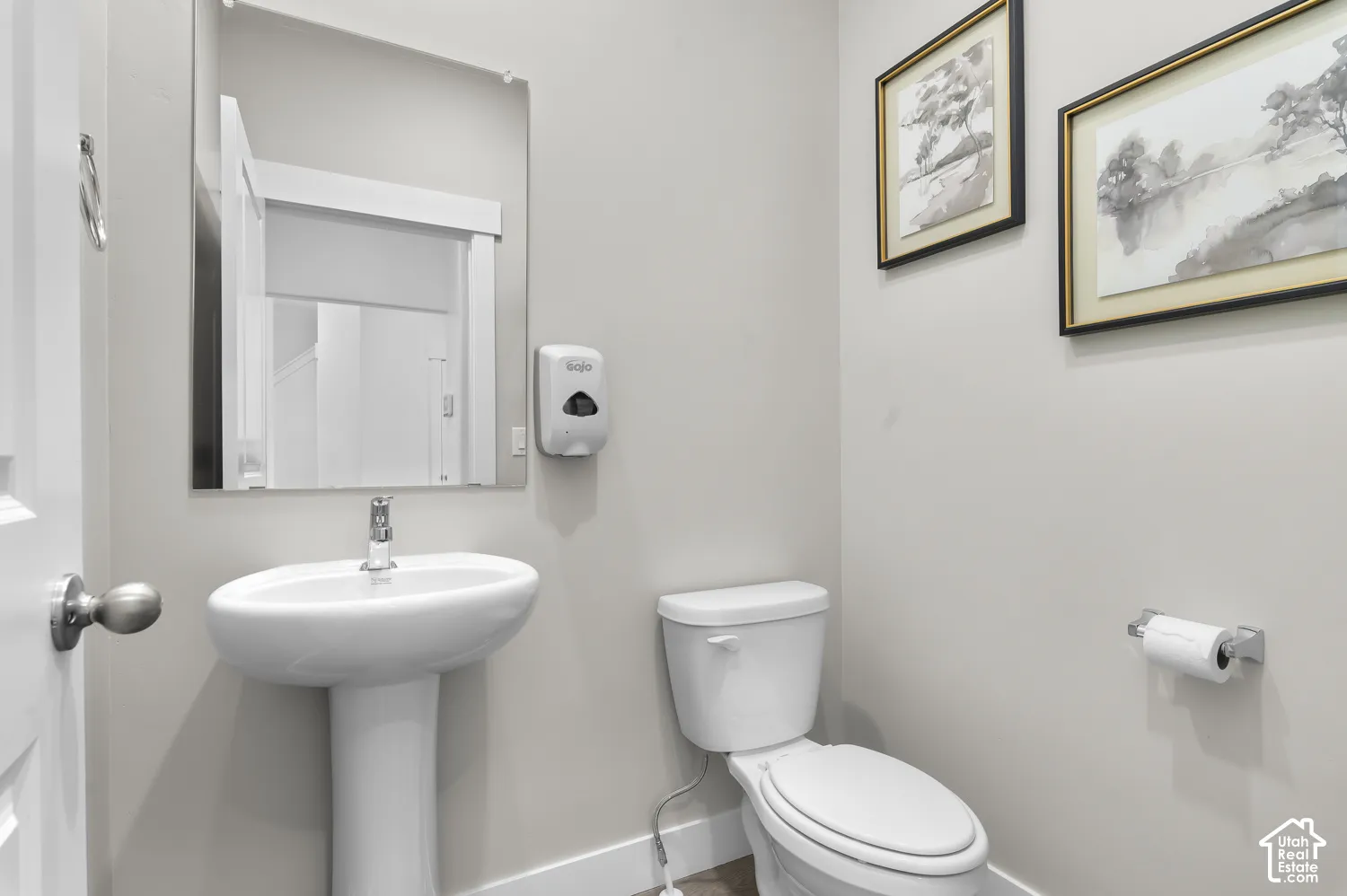 Pedestal sink with a single-handle faucet, frameless wall-mounted mirror, and a standard-height toilet