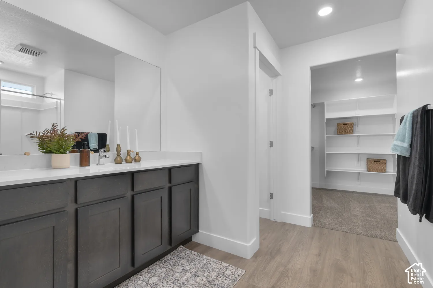 Bathroom featuring a dark wood-finish vanity with a white countertop, large wall-mounted mirror, recessed lighting, and a walk-in closet with built-in shelving