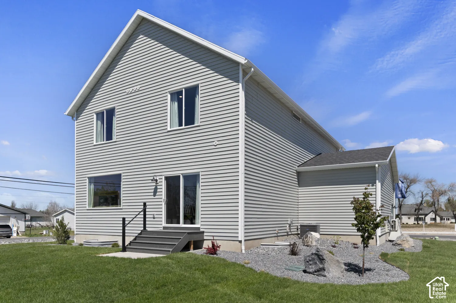 Two-story exterior featuring grey horizontal siding, a gabled roofline, sliding glass door access, an elevated entryway with a black handrail, and low-maintenance rock landscaping