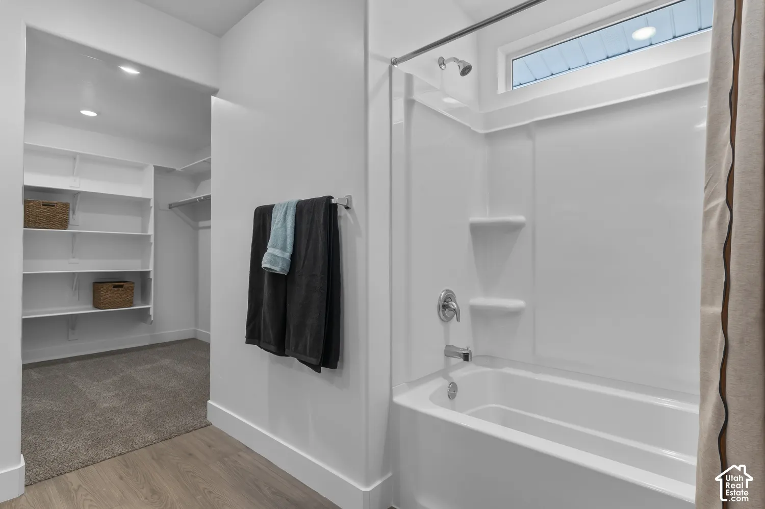 Bathtub and shower combination with a composite surround, transom window, recessed ceiling lighting, and a walk-in closet featuring built-in shelving