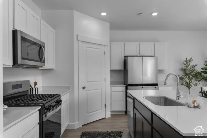 Kitchen featuring white shaker-style cabinetry, a contrasting dark-finish kitchen island, solid-surface countertops, stainless steel appliances, and wood-finish flooring