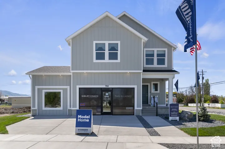 Two-story residence featuring light gray vertical siding, a covered entryway, a concrete driveway, and white window trim