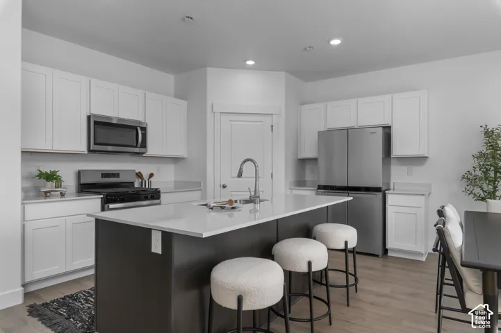 Kitchen featuring white Shaker-style cabinetry, a contrasting dark-finish center island, stone-composite countertops, stainless steel appliances, and recessed ceiling lighting
