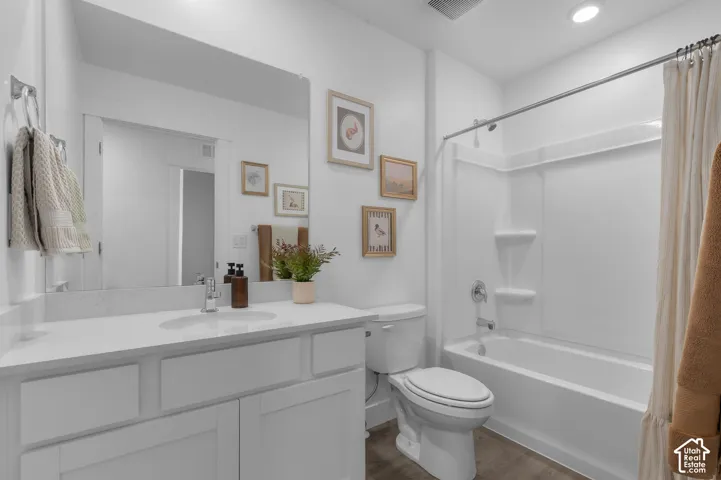 Full bathroom featuring a white vanity with a solid-surface countertop, an integrated sink, a large wall-mounted mirror, a tub-shower combination with a molded surround, and wood-finish flooring