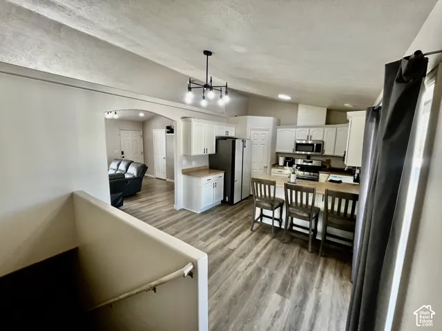 Kitchen featuring white cabinetry, wood-finish flooring, a breakfast bar, and a multi-arm chandelier