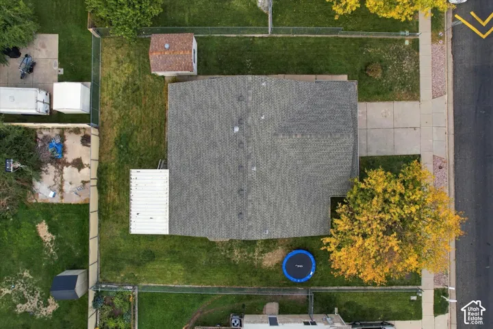 Aerial perspective featuring an asphalt shingle roof, concrete driveway, fenced perimeter, and detached storage shed