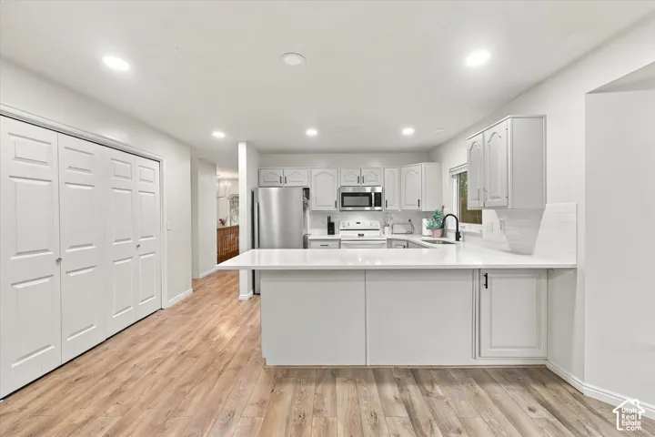 Kitchen featuring light-toned cabinetry, solid-surface countertops, stainless steel appliances, a peninsula with bar seating, and wood-finish flooring