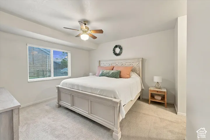 Neutral-toned interior space featuring neutral wall-to-wall carpeting, recessed ceiling tray detailing, and a multi-blade ceiling fan with integrated lighting