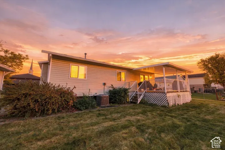Exterior siding, covered deck with white lattice skirting, white metal railing, and lawn