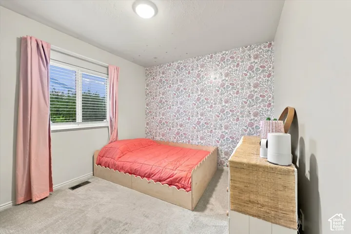Neutral-toned wall-to-wall carpeting, floral patterned accent wallpaper, horizontal blind window treatment, and flush-mount ceiling lighting