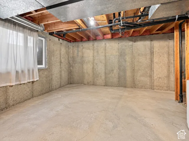 Unfinished storage area featuring poured concrete walls, exposed wood ceiling joists, and a casement window