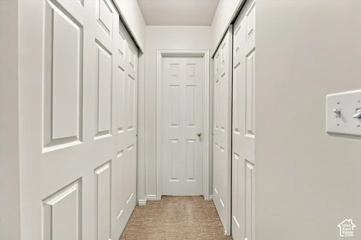 Hallway featuring two sets of floor-to-ceiling sliding panel closet doors, a six-panel swing door with brushed metal hardware, and textured carpeting