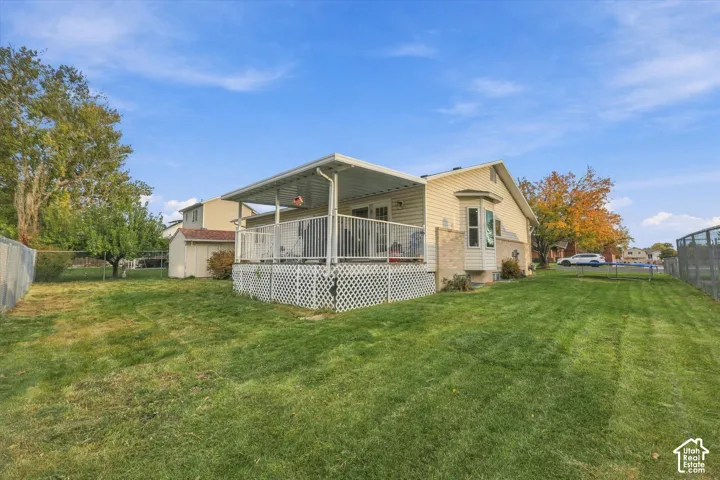 Exterior featuring a covered raised deck with metal railings, lattice skirting, a bay window, and a spacious backyard with a storage shed