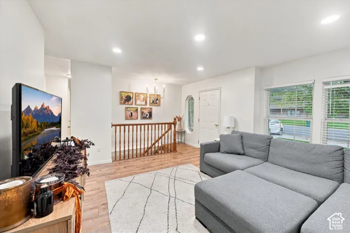 Wood-finish flooring, recessed lighting, stained wood banister with vertical balusters, multi-pane windows with horizontal blinds, and an arched accent window